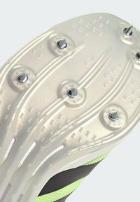 Semelle de crampons de football en plastique blanc translucide, avec six crampons métalliques. Surface texturée avec des lignes en relief et des motifs d'étoiles.