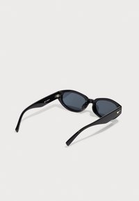 Óculos de sol pretos com um design fino em forma de gato, lentes escuras e armações brilhantes, apresentando um pequeno detalhe metálico nas hastes.