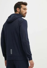 Felpa con cappuccio blu navy caratterizzata da un tessuto testurizzato, maniche lunghe e un accento riflettente con linee orizzontali sul retro.