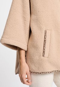 Beżowy polarowy sweter z dużymi rękawami, z kieszenią wykończoną lamówką w leoparda oraz detalem u dołu w leoparda. Miękki, teksturowany materiał.