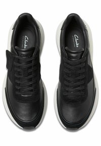 Par av svarta läder- och mockaskor med vita sulor och svarta snören, sedd ovanifrån, varumärkeslogotyp inuti varje sko.