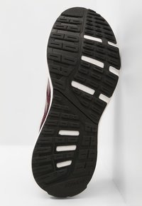 Musta kuminen urheilukengän pohja, jossa on teksturoitu pinta, valkoinen välipohja ja "ADIWEAR" -brändäys.