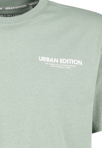 Helles grünes Baumwoll-T-Shirt mit kurzen Ärmeln, geripptem Rundhalsausschnitt und weißem Aufdruck "URBAN EDITION" auf der Vorderseite. Glatte Textur.