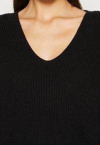 Schwarzer Strickpullover mit V-Ausschnitt, strukturiertem Stoff und formschönem Schnitt, ideal zum Schichten oder als Einzelstück.