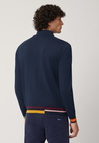 Maglione polo lavorato a maglia blu navy con colletto, maniche lunghe e orlo a righe multicolori. Texture liscia e silhouette aderente.