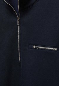 Felpa blu navy con collo alto, dotata di una cerniera argentata sul davanti e di una tasca sul petto con zip, realizzata in tessuto morbido.