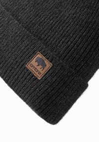 Svart stickad mössa med ribbad textur, som har en fyrkantig brun läderlapp med en bisonikon och varumärkesetikett.