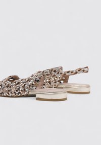 Sandalias trenzadas en dorado metálico y plateado con parte trasera cerrada, tirante en el talón y un tacón bajo bloque para mayor estabilidad.