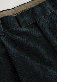 Černá kordurová tkanina s jemnou strukturou, s širokým pasem v kontrastní béžové barvě, překlopeným na vrchu, a hladkou vnitřní podšívkou.