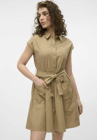 Robe camicia khaki con colletto, maniche corte, vita regolabile con cordoncino e due tasche anteriori. Tessuto morbido e vestibilità ampia.