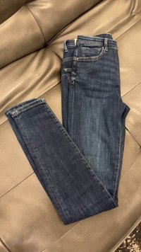 Tmavomodré zložené džínsy z denimu položené na koženú pohovku hnedej farby, zobrazujúce predné vrecká a pútka na opasok.