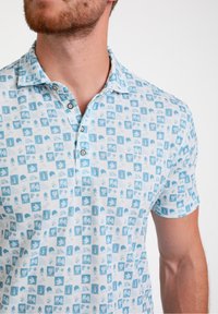Svetlo modra polo majica z vzorcem kvadratov in različnimi ikonami. Mehka tkanina, kratki rokavi in ovratnik s tremi gumbi.