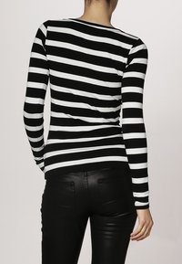 Schwarz-weiß gestreiftes langärmliges Oberteil mit rundem Halsausschnitt, getragen mit eng anliegenden schwarzen Hosen, die einen glatten Stoff und ein figurbetontes Design zeigen.