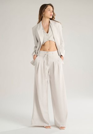 Completo grigio chiaro composto da una giacca corta con bottoni e pantaloni a gamba larga con vita elastica e dettagli plissettati.