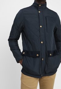 Námořnický prošívaný kabát se zlatými patentkami, vysokým límcem, kordovou úpravou na kapsách a elegantním, přiléhavým střihem.