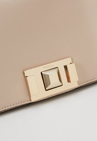 Borsa a mano in pelle beige con una prominente chiusura in metallo dorato con un accento quadrato, texture liscia e un sottile motivo a grana.