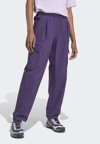 Purple cargo pants with an elastic waistband, pleats, and side pockets, made of lightweight fabric. Worn with gray and purple hiking shoes.
