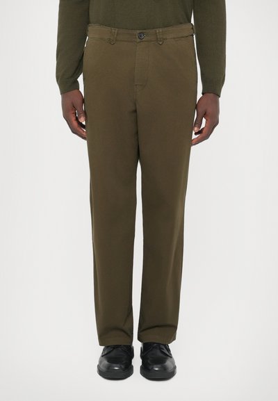 Man wearing olive green straight-leg pants, dark green long-sleeve shirt, and black leather shoes standing against a white background.