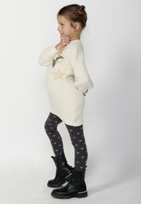 Suéter blanco de punto con un diseño de estrella, combinado con leggings gris oscuro que presentan patrones de corazones dorados y botas negras hasta el tobillo.