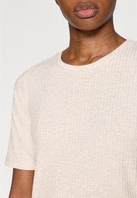 Μπεζ ριγωτό κοντομάνικο μπλουζάκι με στρογγυλή λαιμόκοψη και κοντά μανίκια. Το ύφασμα φαίνεται μαλακό, με διακριτική υφή και άνετη εφαρμογή.