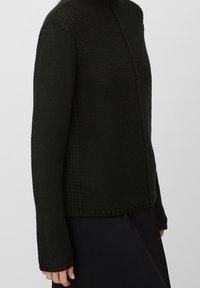 Stickad tröja i mörkgrön, med hög hals, långa ärmar och en strukturerad mönstring med ribbade detaljer längs kanterna.