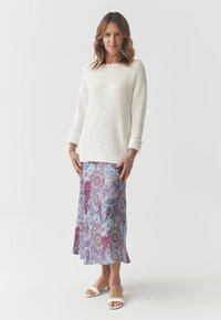 Pull en maille blanche à manches roulées, associé à une jupe à motifs paisley bleus et roses. La mannequin porte des sandales blanches à bout ouvert.