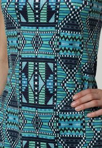 Abito a fantasia in teal, blu navy e nero caratterizzato da forme geometriche, righe e un tessuto testurizzato con una silhouette aderente.