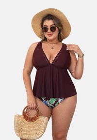 Bordeaux badmode top met een uitlopende vorm, gecombineerd met een bloemenprint onderstuk. Accessoires zijn een ronde strooien tas en een zonnebril.