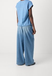 Blå denimtop med korte ærmer og snoretræk i taljen, parret med vide denimbukser med en lys til mørk gradient og synlige sømme.
