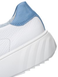 Nahaufnahme der Ferse eines weißen Sneakers mit strukturiertem Leder, blau gepolstertem Kragen und dicker weißer gerillter Sohle.