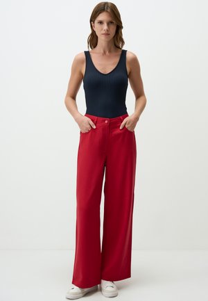 Red wide-leg trousers with a button closure and side pockets, paired with a fitted navy ribbed tank top. Smooth fabric texture.