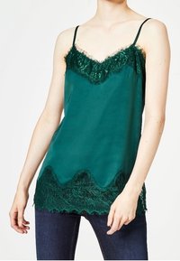 Grön satin camisole med spetsdetaljer vid halsringning och fåll, med justerbara axelband och en vågformad kantdesign.