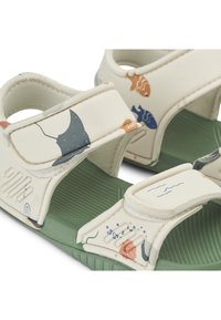Light-colored sandals with adjustable velcro straps and a textured green sole. Features marine-themed patterns in various colors.