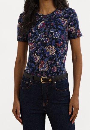 Haut bleu marine à manches courtes présentant un imprimé floral rouge, blanc et bleu avec un col rond. Associé à un jean denim foncé et une ceinture noire.