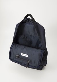 Navy fabric backpack with a zip opening, featuring an interior pocket and adjustable straps. Smooth texture with minimal hardware accents.