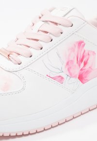 Baskets blanches avec lacets rose clair et motif floral rose sur le côté, avec une semelle blanche et une semelle extérieure rose clair.