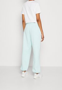 Světlé modré, volné tepláky s elastickým pasem a manžetami. V kombinaci s bílým tričkem s krátkým rukávem a bílými teniskami.