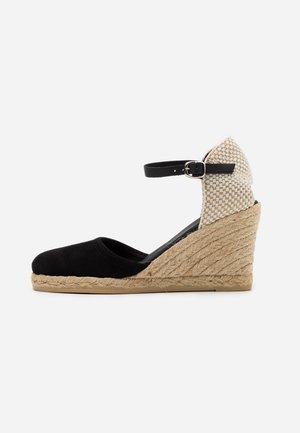 Espadrille à talon compensé noir avec un talon en jute tressé, dos texturé beige, bout fermé et bride de cheville noire avec boucle en argent.