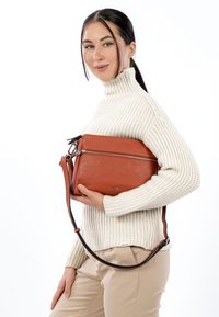 Brown leather handbag with two zippered compartments, adjustable strap, and embossed branding. Structured shape with a smooth texture.