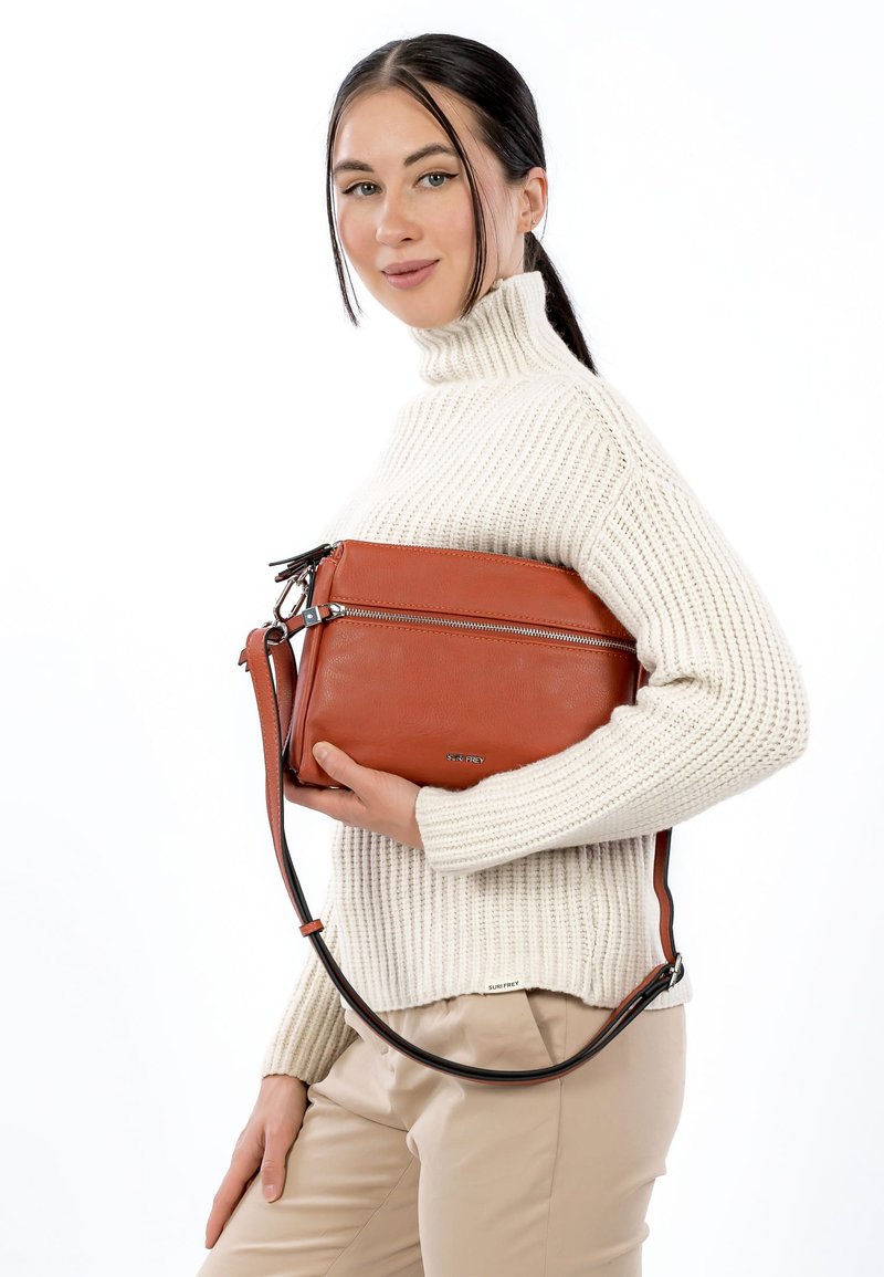 Brown leather handbag with two zippered compartments, adjustable strap, and embossed branding. Structured shape with a smooth texture.