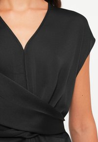 Black blouse featuring a V-neck design, short sleeves, and wrap-style waist. Made from a smooth, lightweight fabric with a subtle texture.