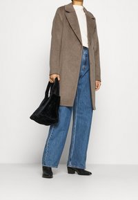 Bruine wollen jas met een omgeslagen revers, gecombineerd met hooggesneden blauwe spijkerbroeken. Een kleine zwarte nepbont handtas en zwarte leren laarzen met hak maken de look compleet.