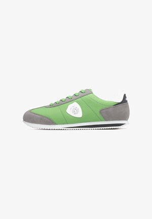 Zapatilla verde y gris con parte superior de tela lisa, suela de goma, forma redondeada y detalles en blanco. Presenta un detalle de logo circular en el lateral.