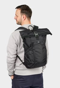 Zaino nero con chiusura a rotolo, spallacci regolabili, un ampio scomparto principale, tasca frontale e lati ripiegabili per una maggiore capacità di stoccaggio.