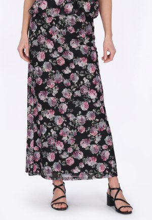 Kvinde iført en sort blomsterprintet maxinederdel med pink og grå blomster, kombineret med sorte remsandaler med blokhæl.