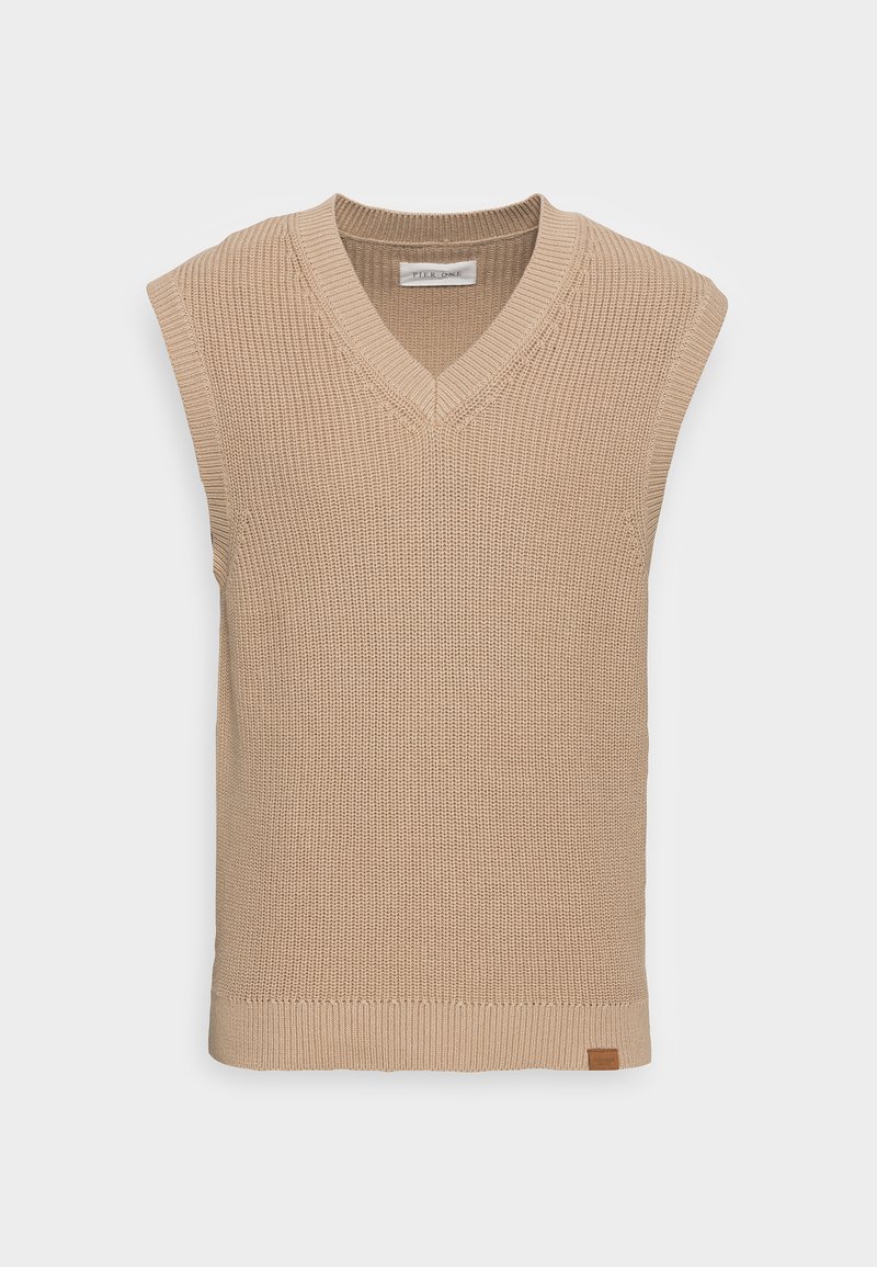 Gilet sans manches en tricot beige avec un décolleté en V, texture côtelée et une petite étiquette en cuir en bas à gauche.