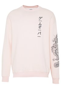 Sudadera de color rosa claro hecha de una tela suave, con un gran gráfico de un dragón negro en una manga y texto en japonés en el lado opuesto.