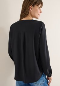Blouse noire à manches longues avec une coupe décontractée, encolure ronde et détails de plis subtils au dos. Texture lisse, associée à un bas en denim.