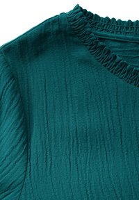 Teal topp med en texturerad tygkvalitet med subtila vertikala linjer, samlad halsringning och en mjuk, lätt skrynklig yta.