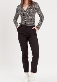Chemise à motifs noir et blanc à boutons, manches longues, associée à un pantalon noir et des baskets blanches. Ceinture accentuant la taille.